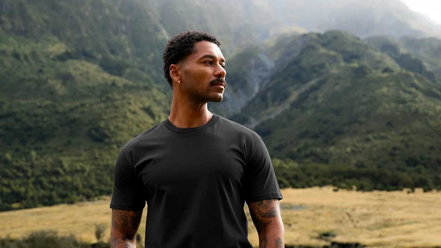 AS Colour black eco-friendly t-shirt on a model outdoors in a mountain landscape.