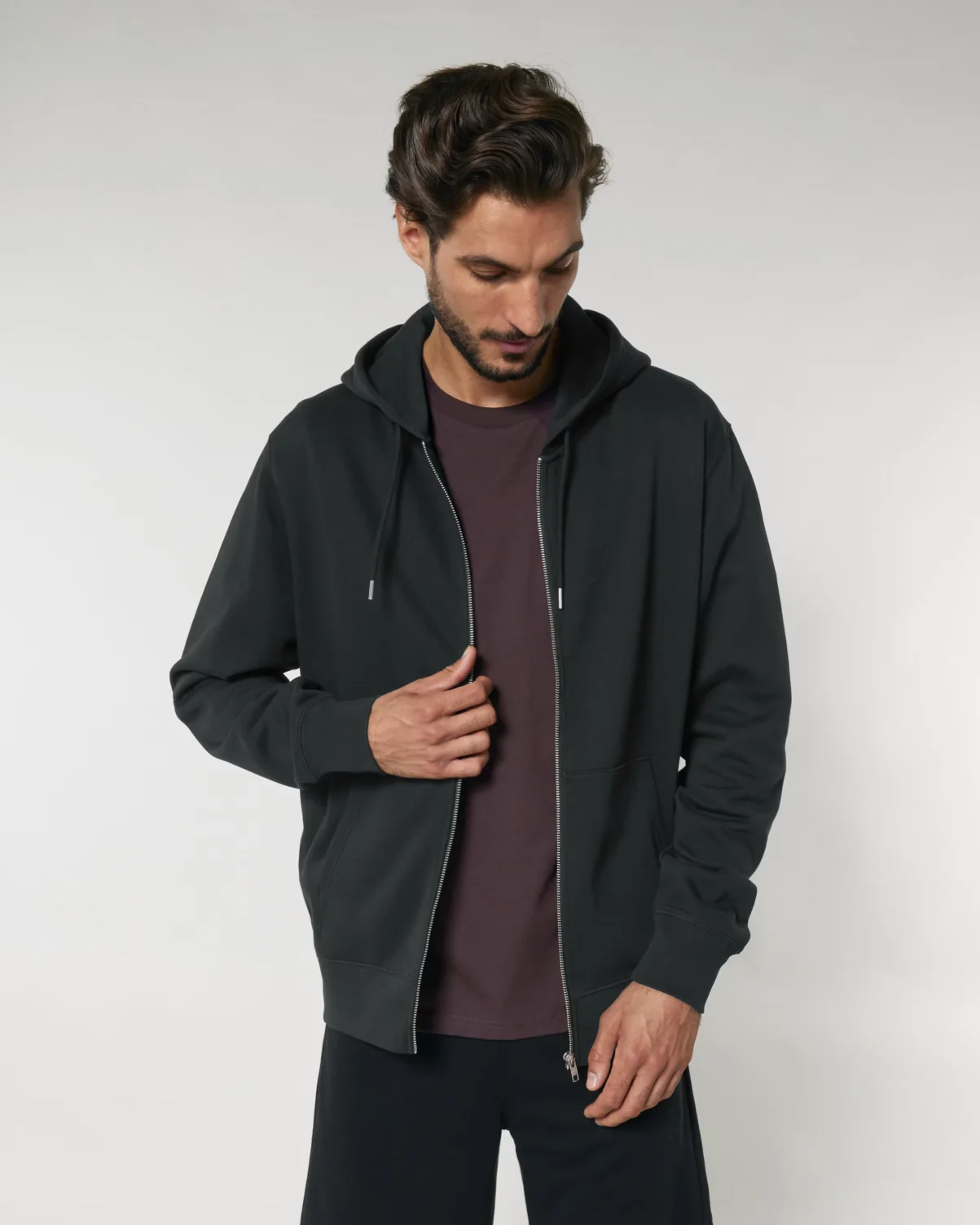 A male model wearing the eco-friendly Stanley/Stella Cultivator 2.0 Zip-Up Hoodie in black. It has a relaxed fit and clean, heavyweight look.